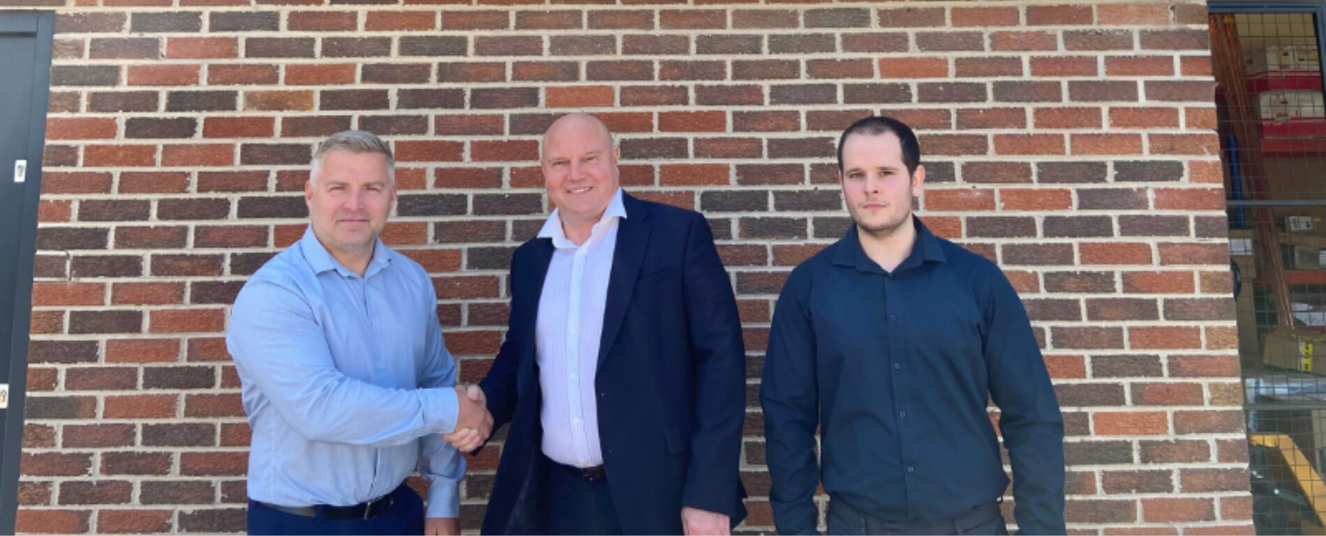 Three men stood outside a building shaking hands